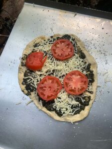 Basil pesto pizza with tomatoes from the garden--ready to go in. Lots of cornmeal on the bottom means that it will transfer effectively to the peel and into the oven. 